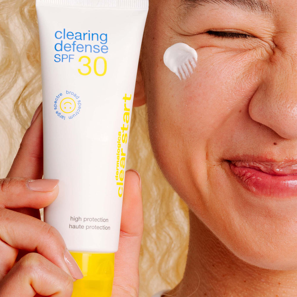 Person applying sunscreen cream to their face with a tube labeled 'Clearing Defense SPF 30' in the foreground.
