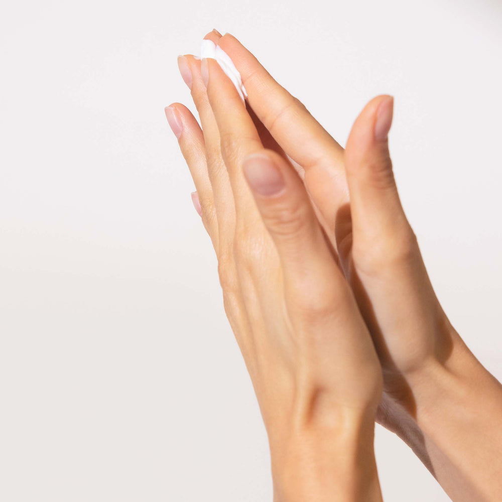 Close-up of two hands with light skin and clear nail polish on a plain background
