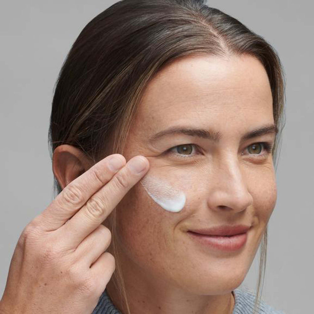 Woman applying powerbright overnight cream to her face with a neutral background