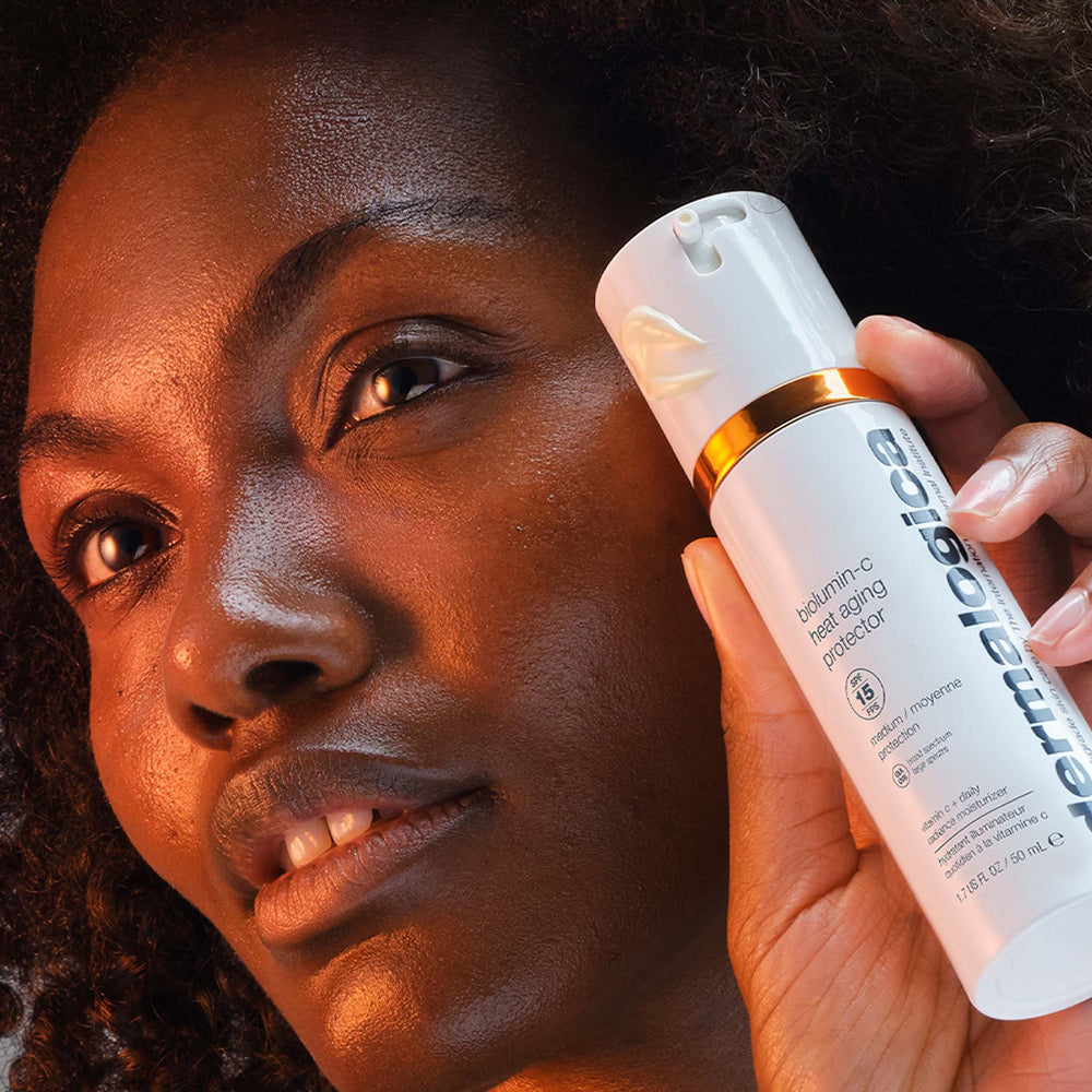 Woman holding a biolumin-c heat aging protector spf15 close to her face